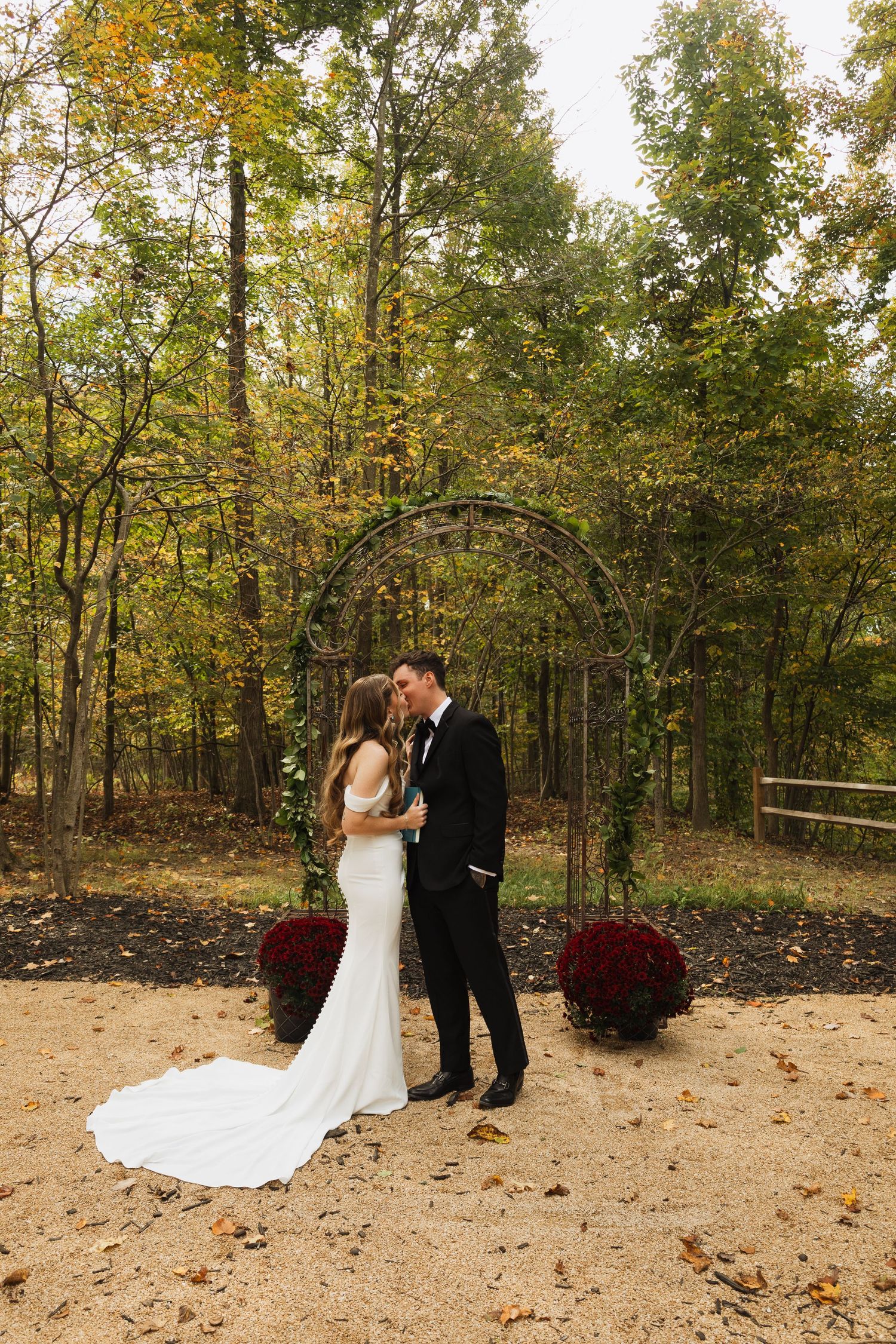 A couple shares an intimate moment on a forest path decorated with burgundy mums for their autumn wedding.