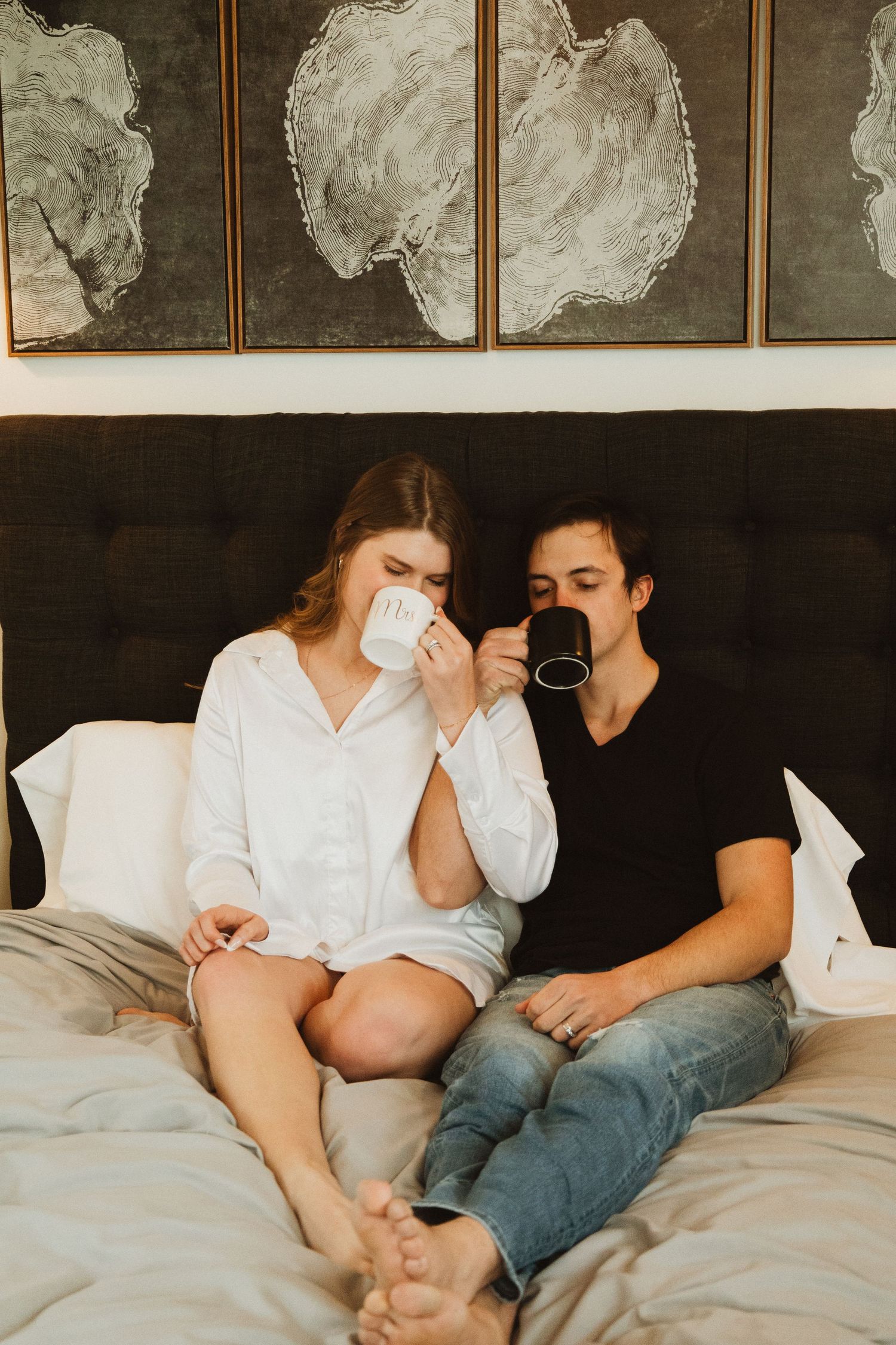 Couple sharing morning coffee in bed beneath abstract wall art and crystal chandelier.