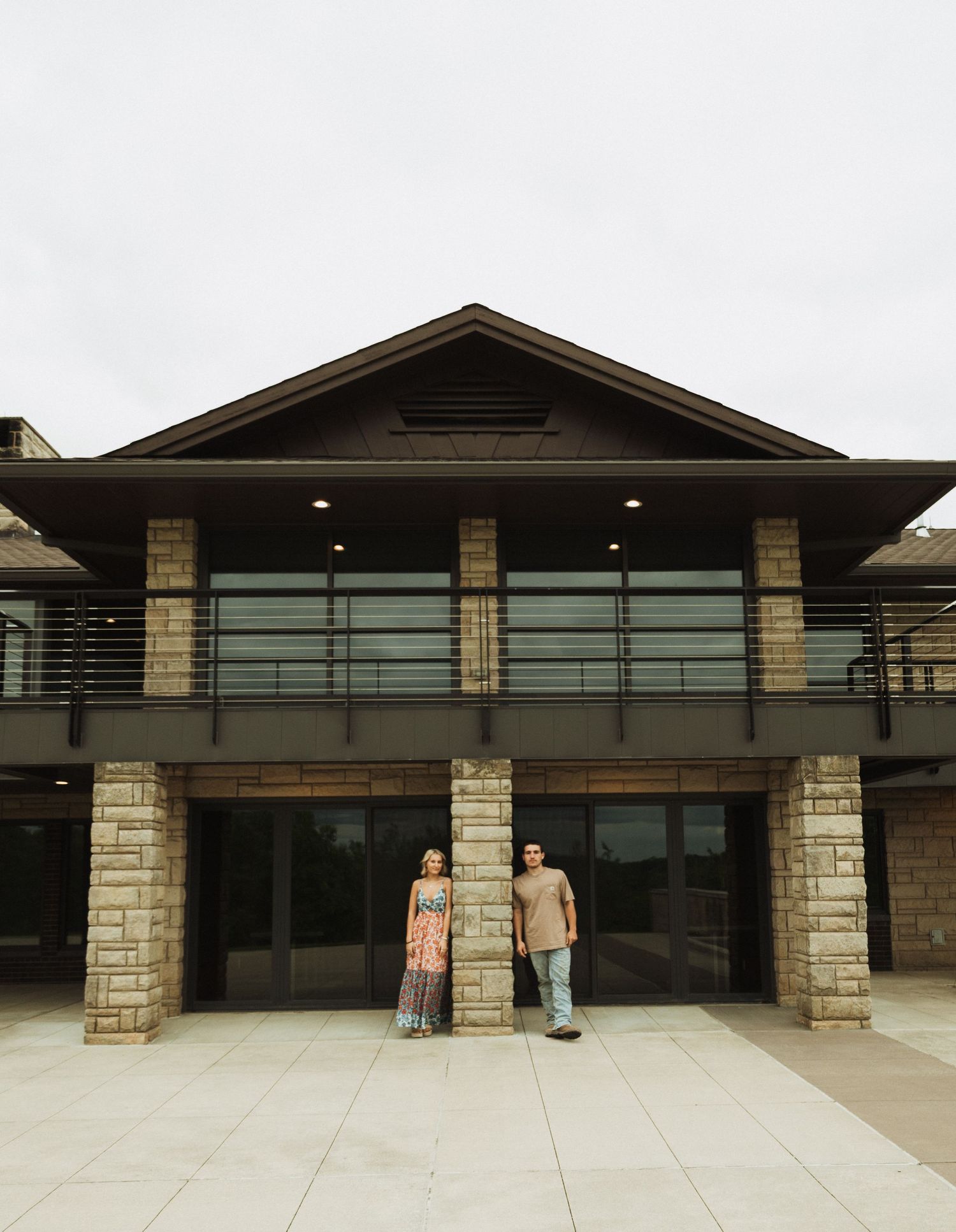A couple stands in front of a modern building with stone pillars and glass windows.