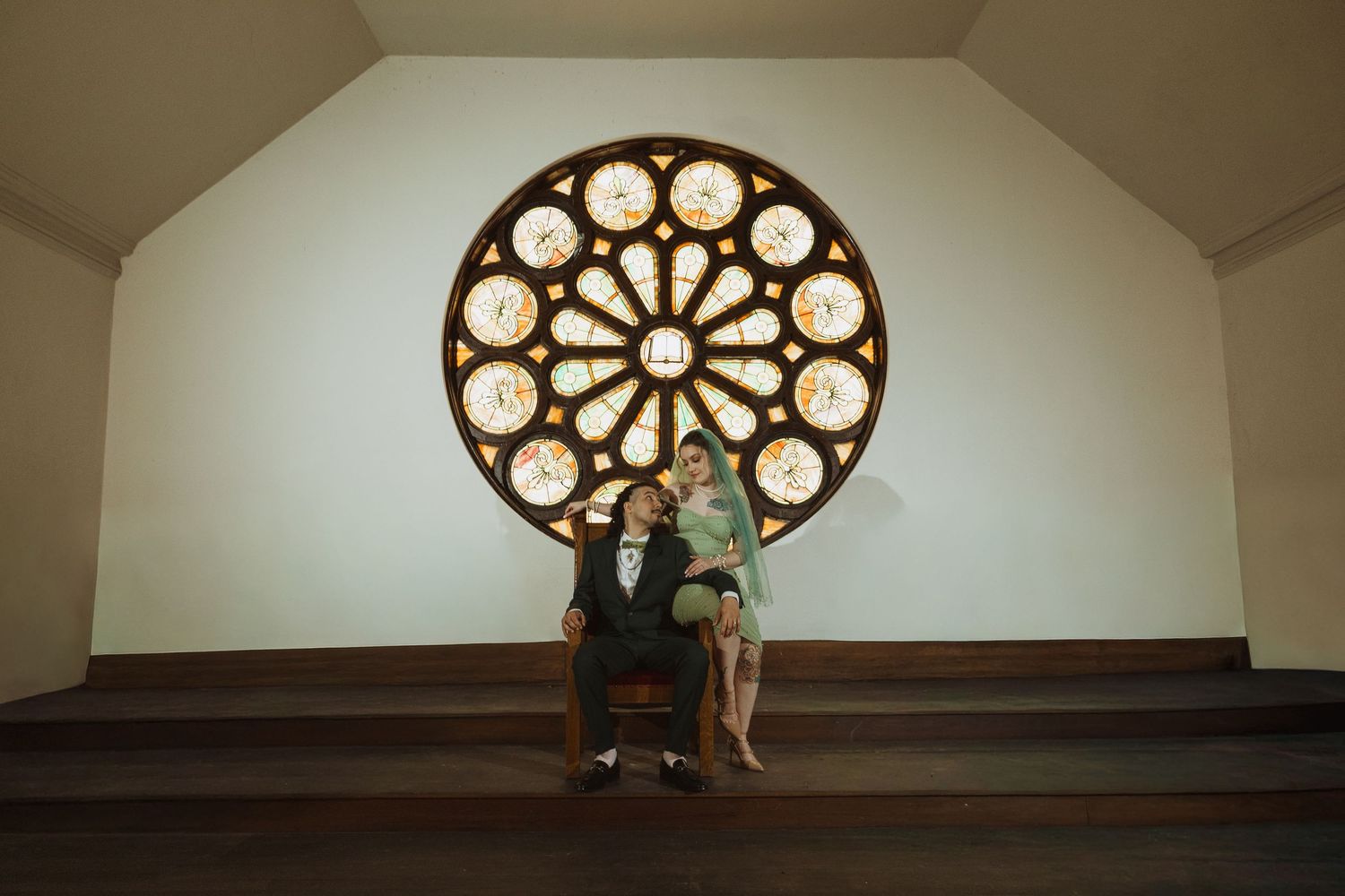 Bride and groom sit together beneath a stunning stained glass rose window in a historic church.