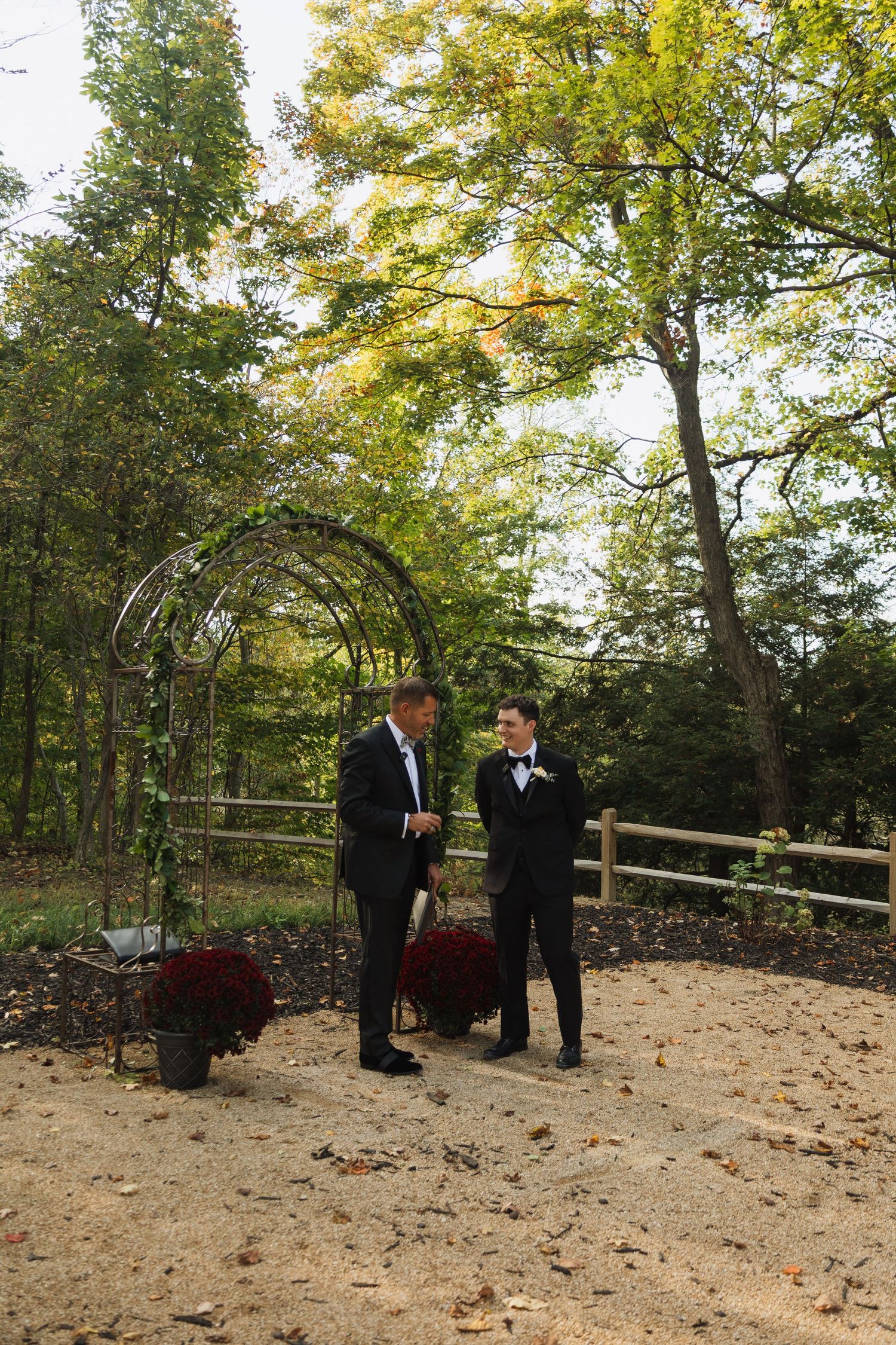 Wedding ceremony in a wooded outdoor setting with fall foliage and wooden fencing.