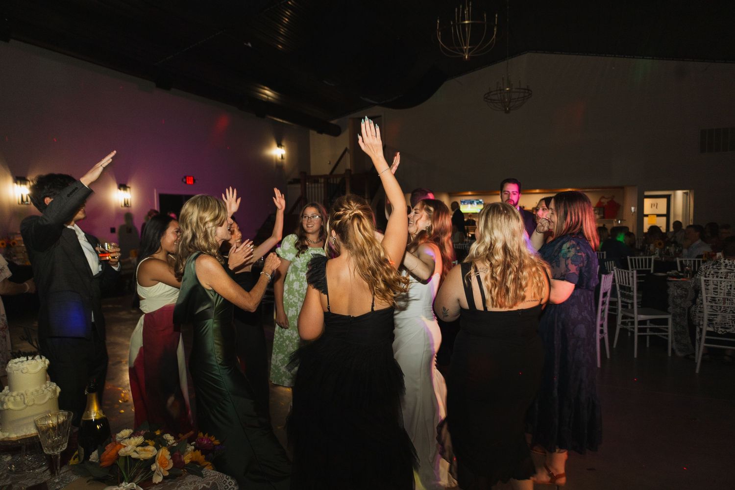 Wedding reception dance floor filled with guests celebrating under dim lighting.