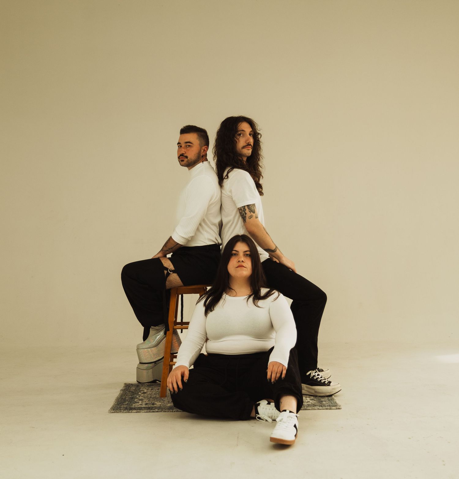 Three people in matching white tops and dark pants posing together on patterned rug in studio setting.