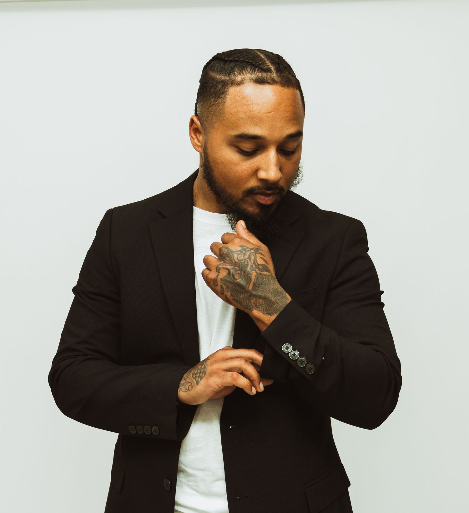 Professional photo of someone in black suit jacket and white shirt adjusting their cuff sleeve while showing hand tattoos.