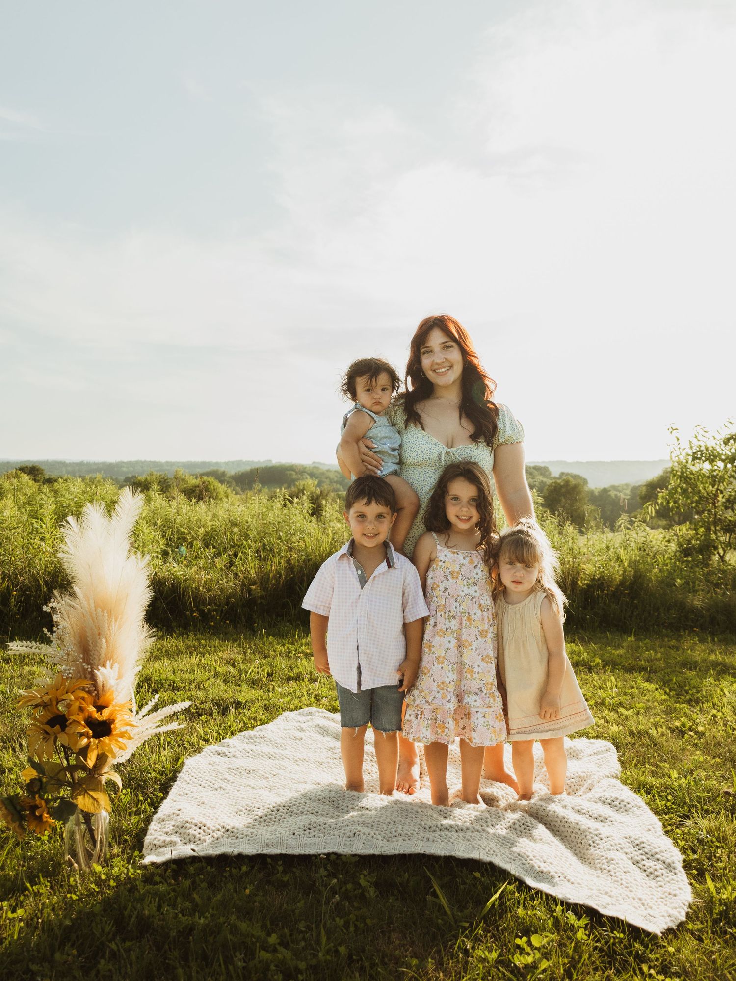 Group portrait of family members relaxing on a white blanket in a grassy field at sunset.