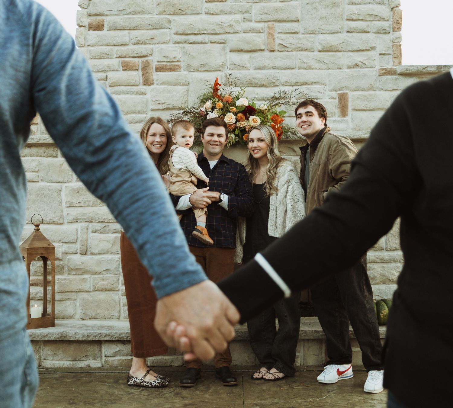 Family members share a candid moment against a stone wall backdrop with lantern decorations.