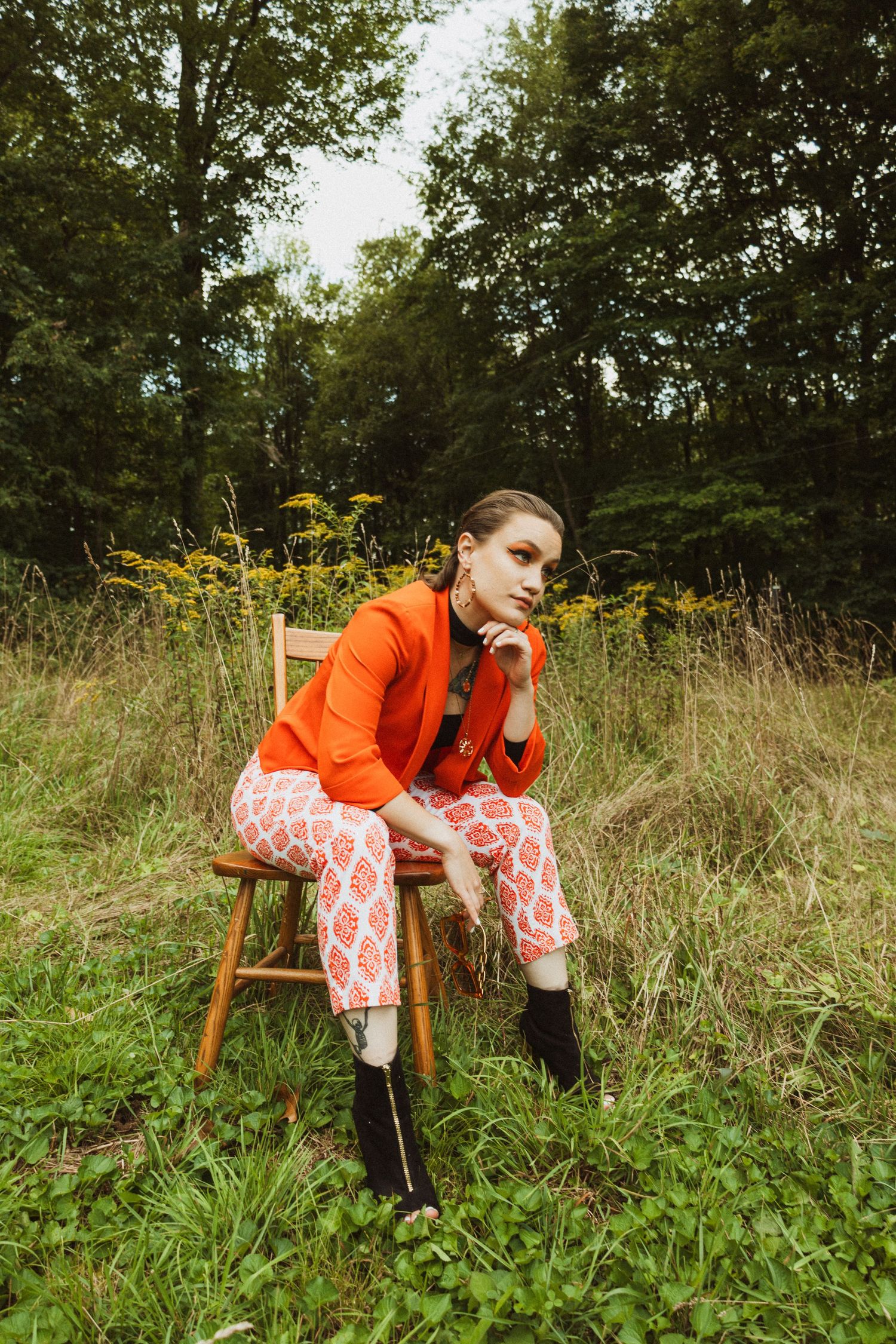 Vintage-inspired fashion pose on wooden chair amidst wild flowers and tall grass.