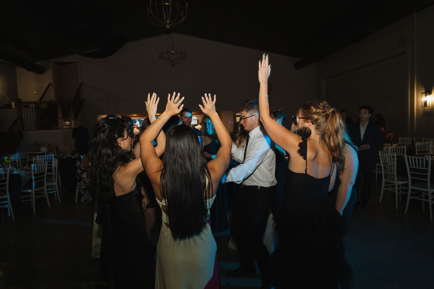 Wedding reception dance party with silhouetted guests raising hands on dark dance floor.