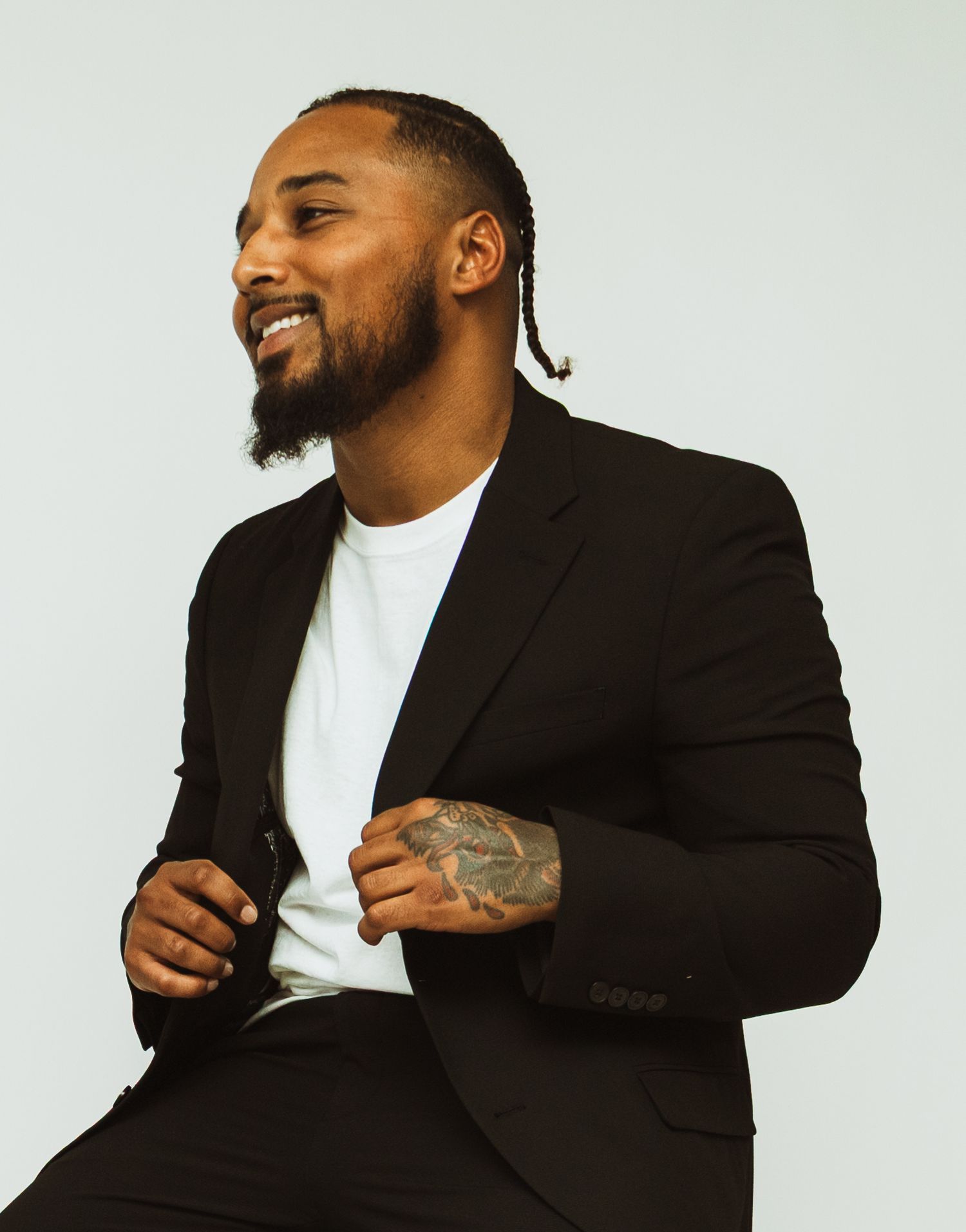 Person in black blazer and white t-shirt smiling while sitting against light backdrop.