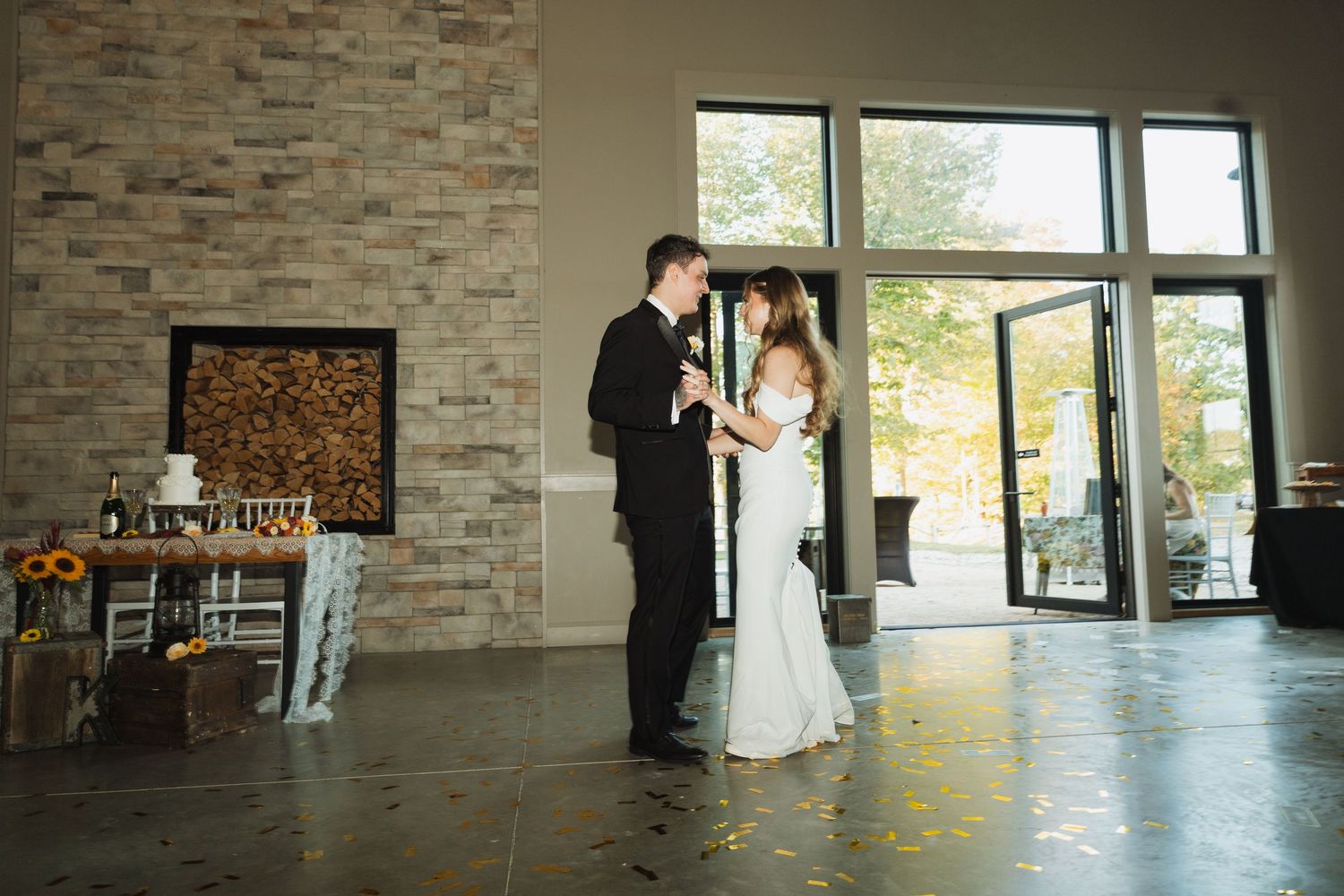 A couple shares an intimate moment in a modern venue with stone walls and stacked firewood.