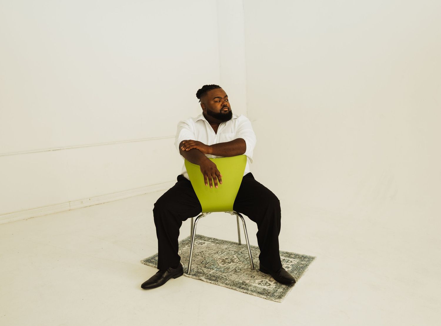 A person sits on a neon yellow chair against a white background with a small rug underneath.