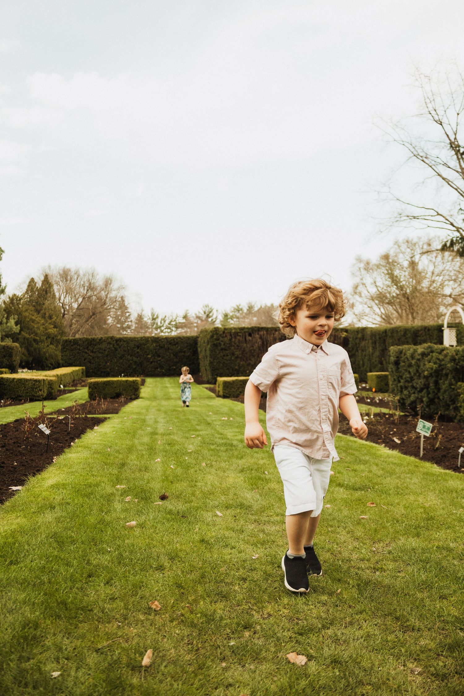 A child runs joyfully across a well-manicured garden lawn on a cloudy day.