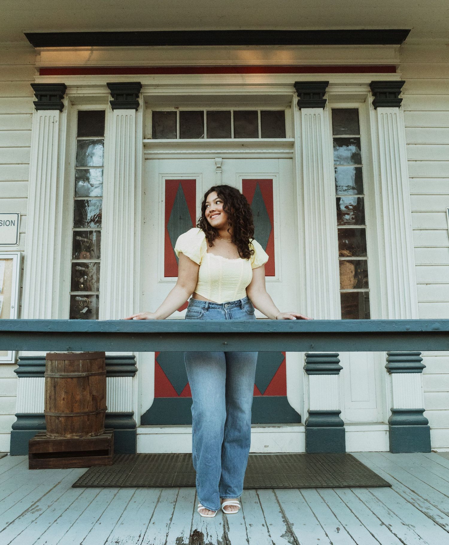Casual portrait on white porch with classical columns and red doors in background.