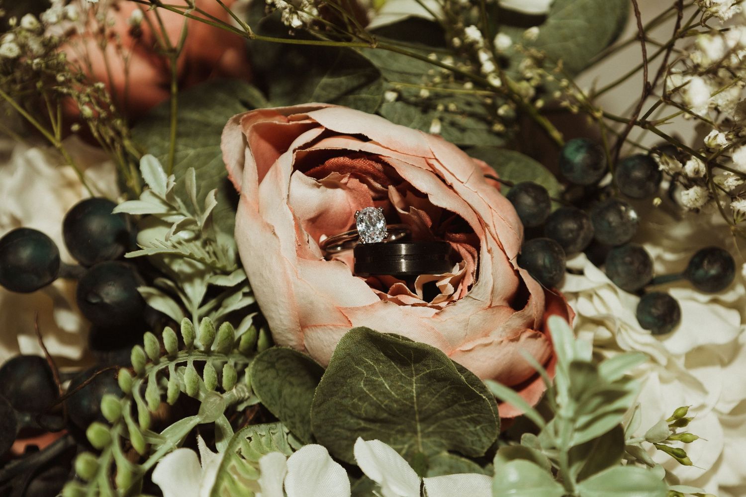 Close-up of a pink garden rose with greenery and dark berries in a floral arrangement.