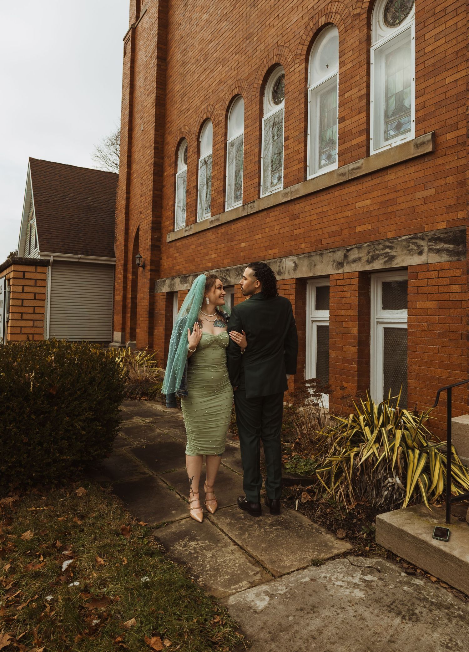 Bride and groom sharing a kiss outside a red brick church on a cloudy winter day.