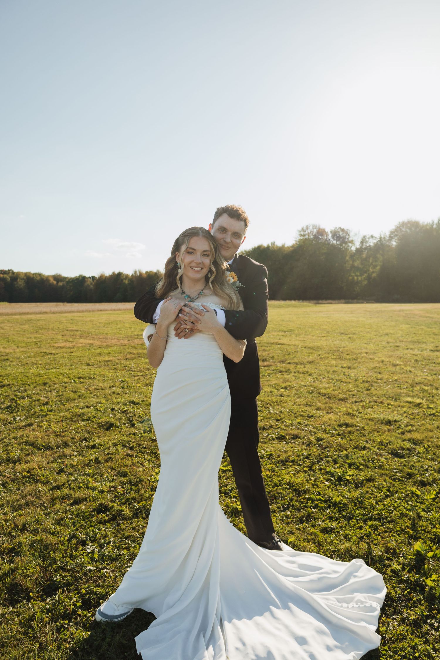 A couple in wedding attire dances and spins in a sunlit meadow at golden hour, the bride's white dress flowing gracefully.