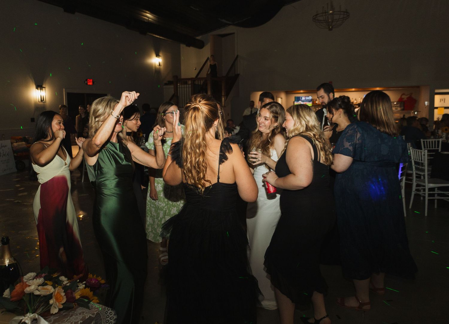 Wedding guests dancing together on a dimly lit dance floor at an evening reception celebration.