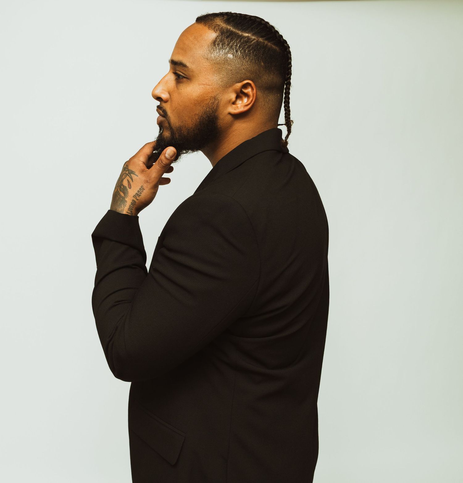 Side profile portrait of someone in a dark blazer with a contemplative pose against white backdrop.