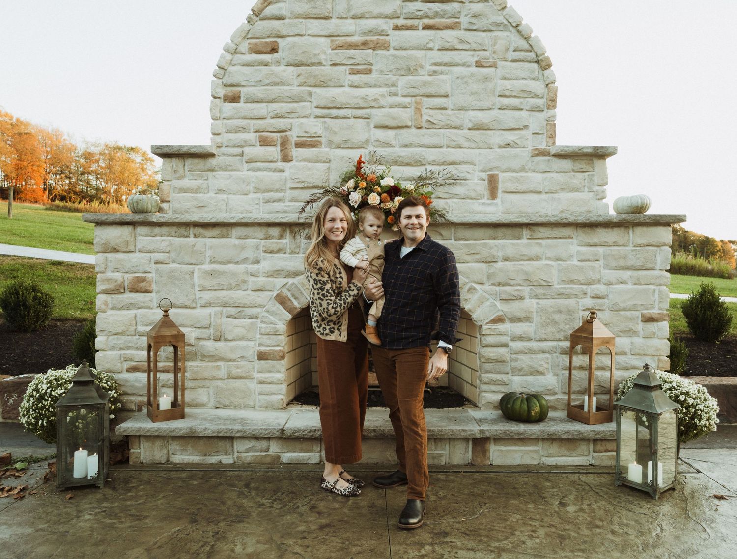 Couple poses in front of stone wall decorated with autumn flowers and lanterns.