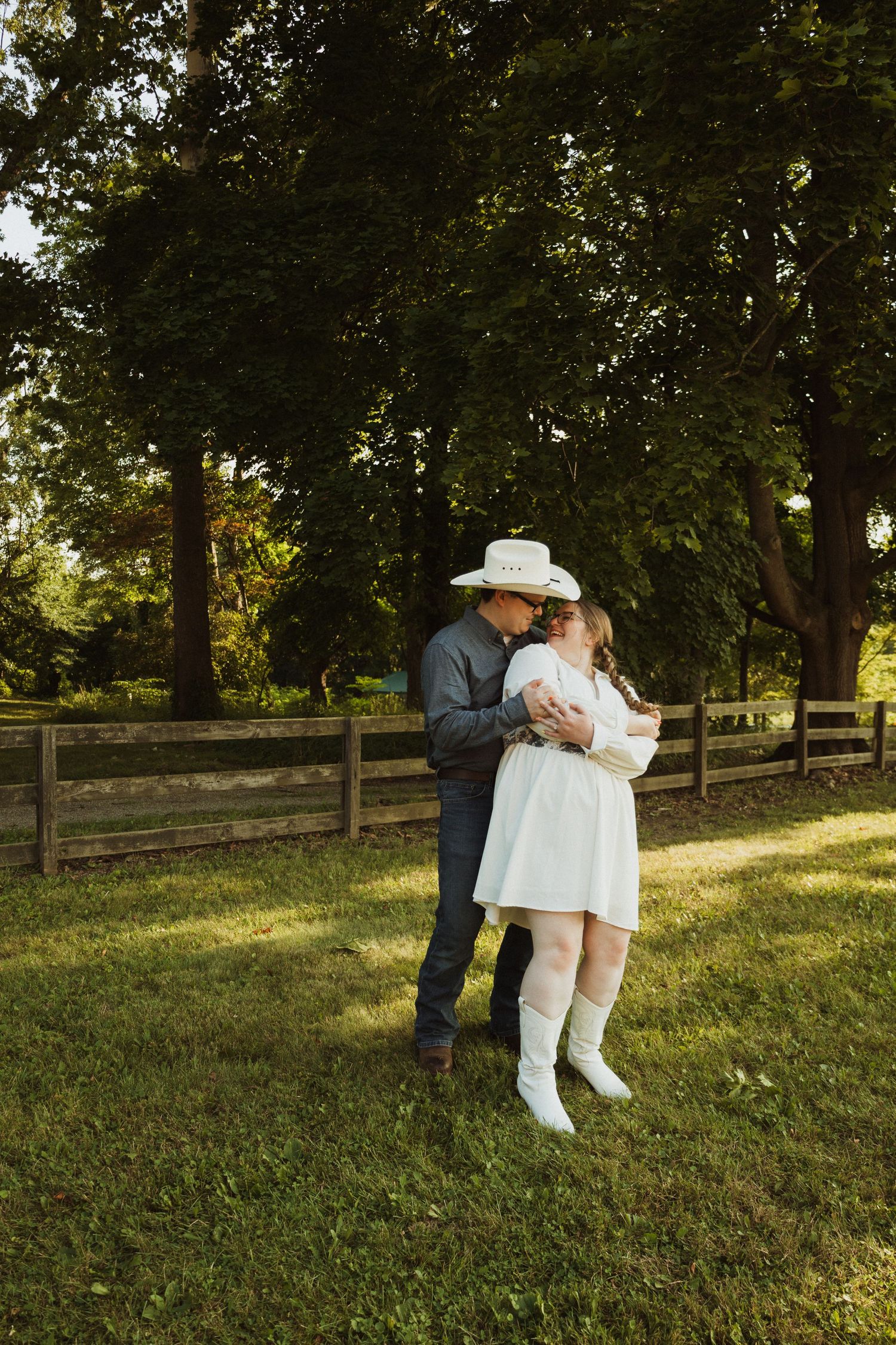 Sunset engagement photography featuring western-styled couple in playful poses on grassy hill.