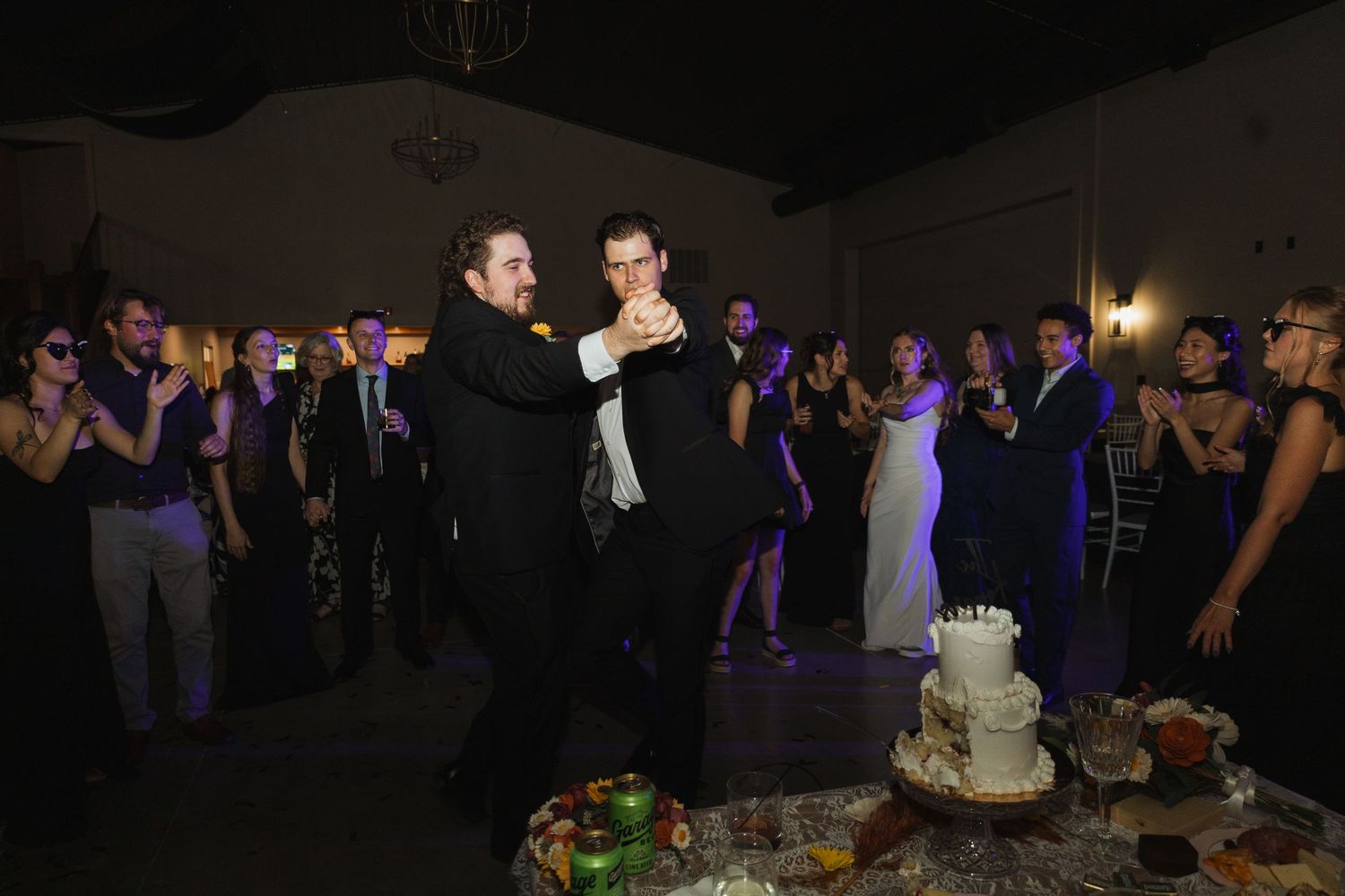 Wedding guests dance and celebrate on a dimly lit dance floor during an evening reception celebration.