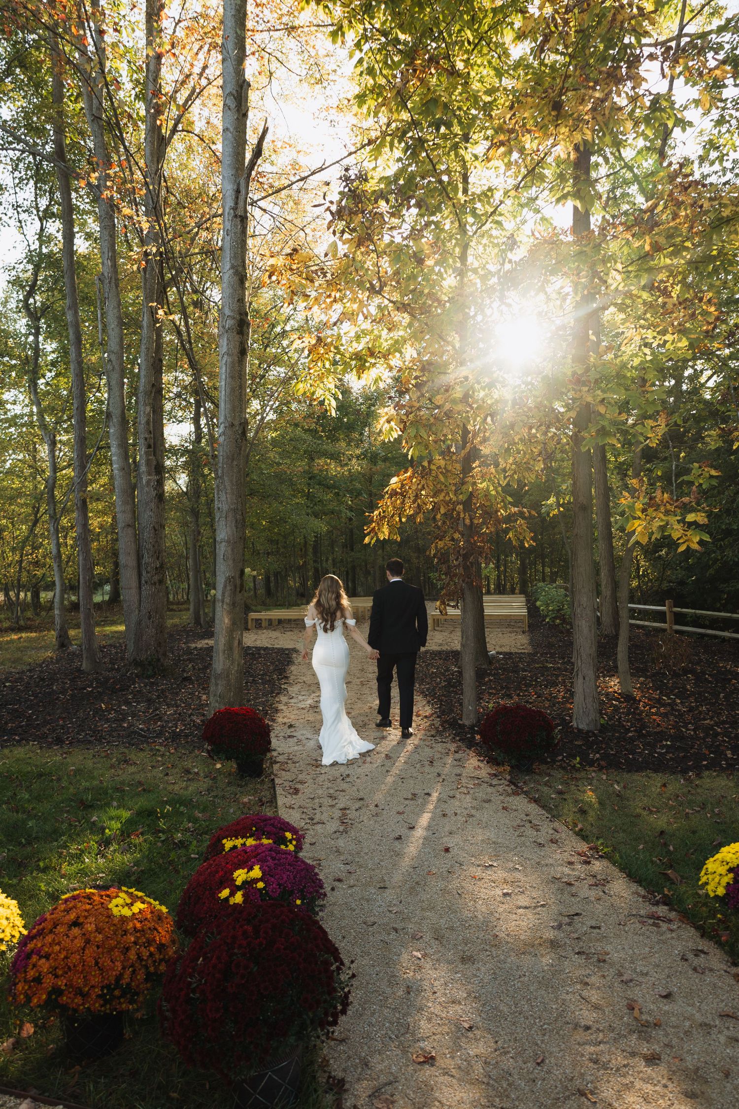 Newlyweds walking along a fall garden path decorated with colorful mums.
