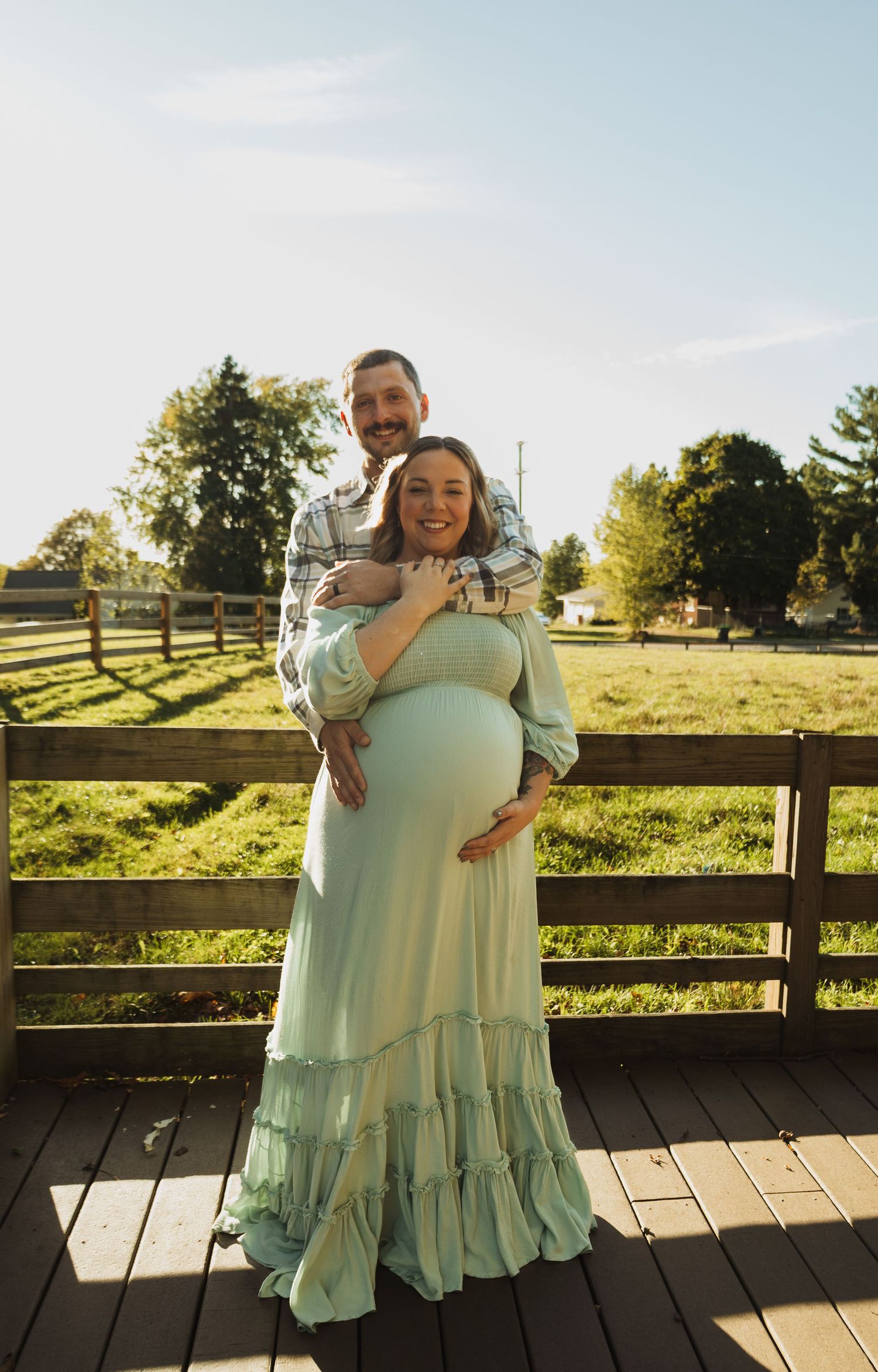 A series of four photos showing a tender embrace between two people in matching mint green dresses on a wooden deck.