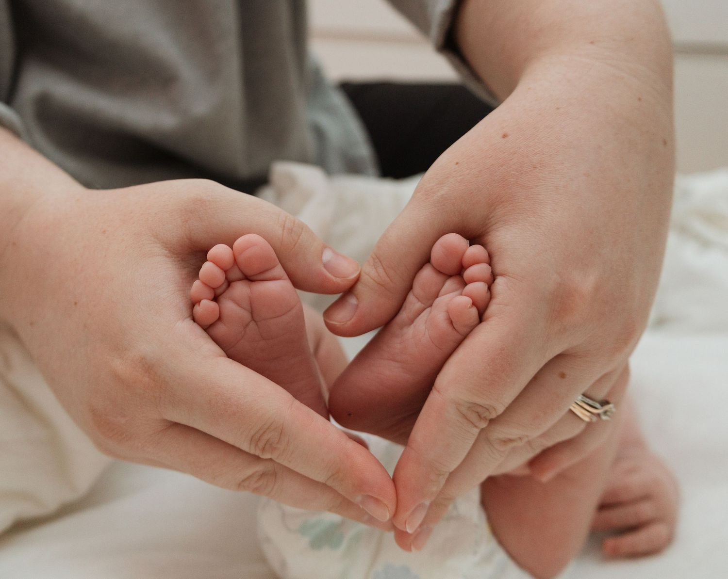 Gentle hands cradle tiny newborn baby feet forming a heart shape on soft white fabric.