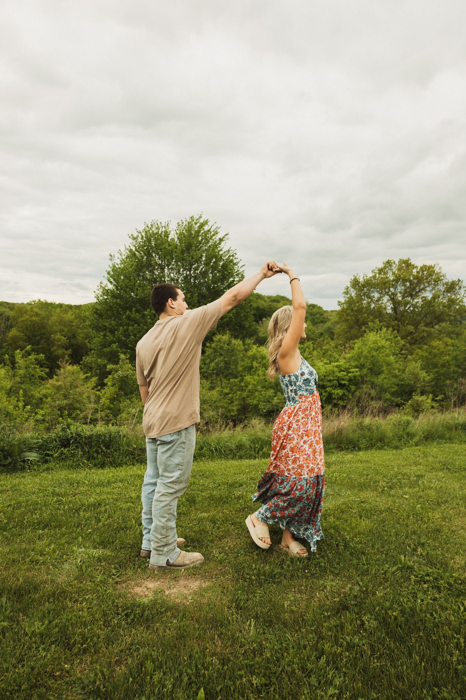 A couple dancing and twirling together on a hilltop with lush greenery in the background.