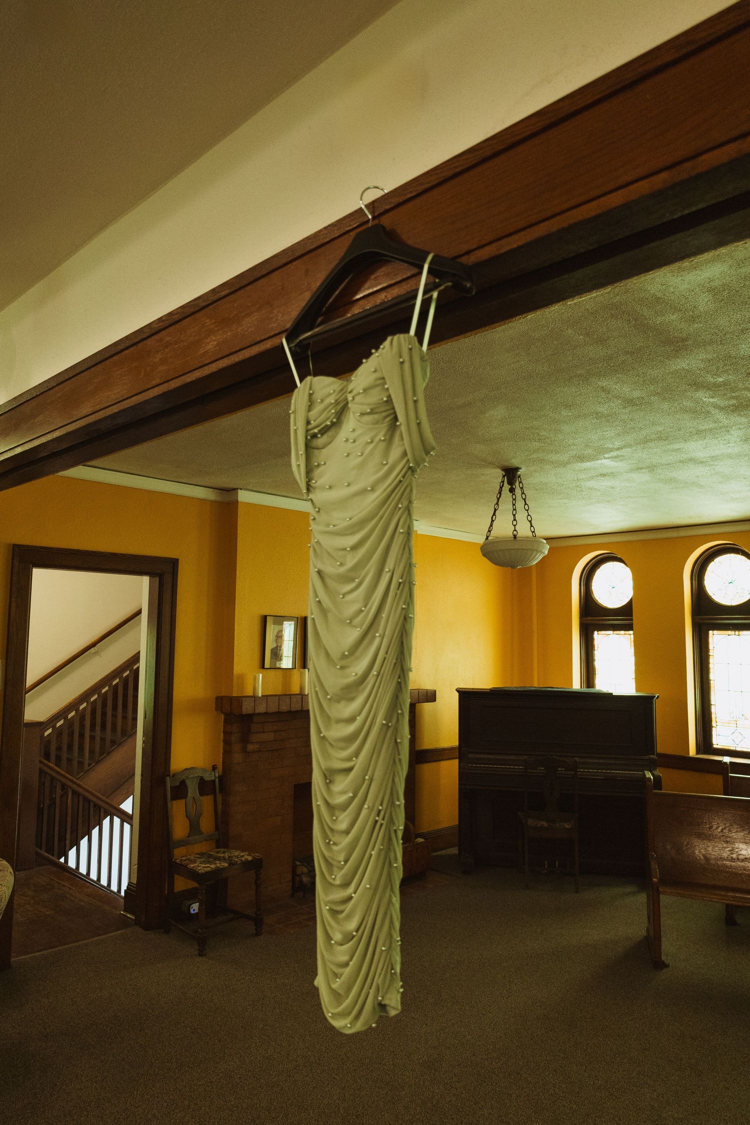 Elegant sage green wedding dress hanging on wooden beam in vintage church room with piano.