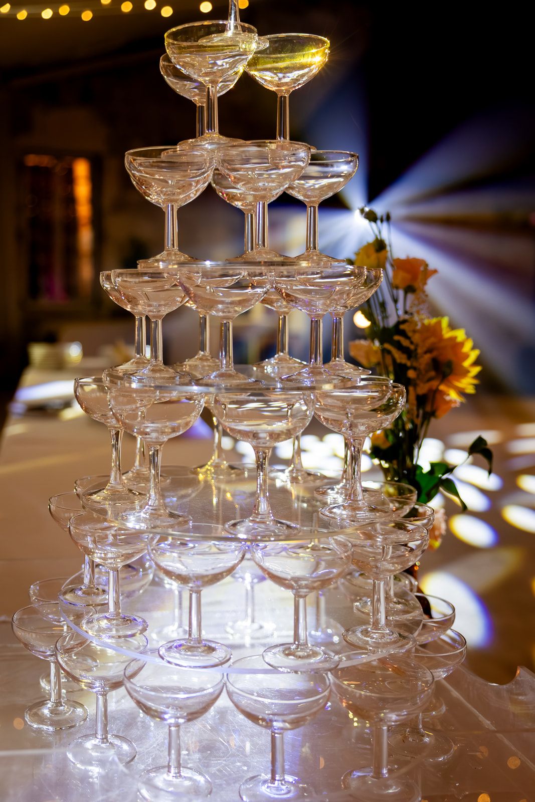Elegant champagne tower with stacked coupe glasses glowing under warm lighting at an upscale event.