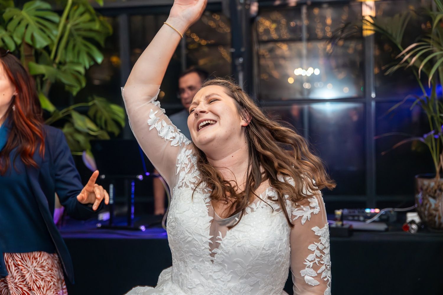 Dancing figures in wedding attire celebrate joyfully on a dimly lit dance floor with tropical decor.