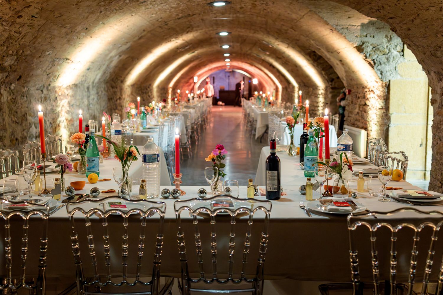 A panoramic view of an ancient stone wine cellar with arched ceilings and rows of wine barrels in dim lighting.