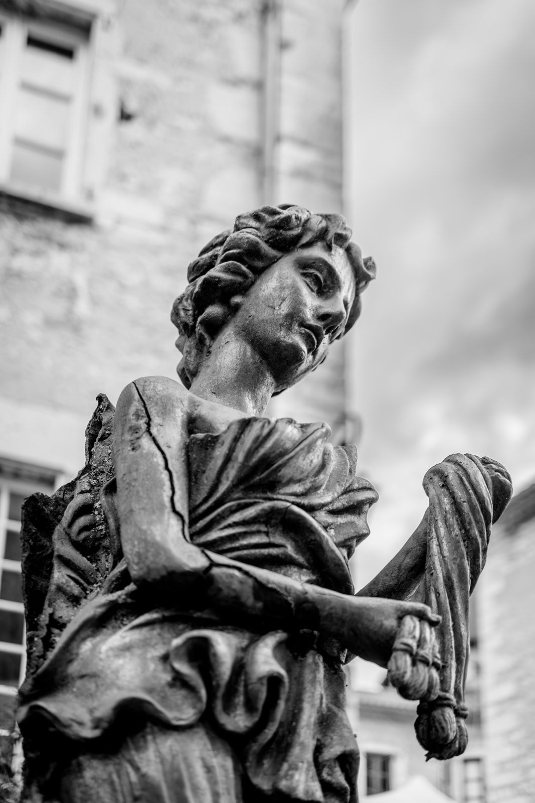 Black and white photo of a classical stone statue holding a scroll, captured from a dramatic low angle.