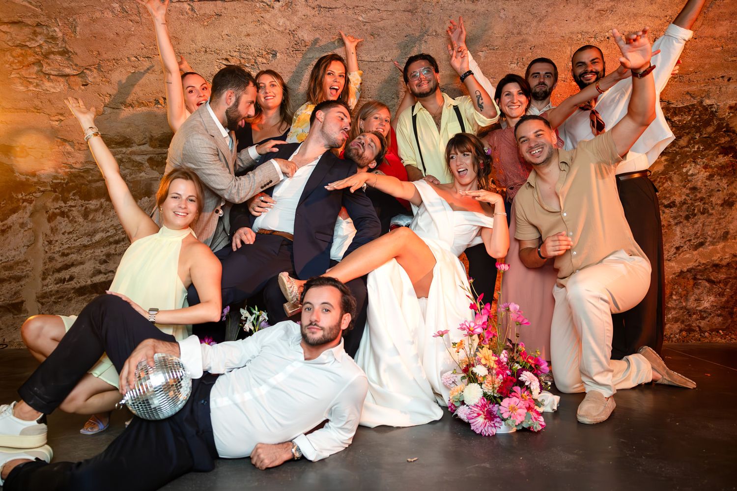 A group of wedding guests pose together on stone steps in a rustic venue during a celebration.