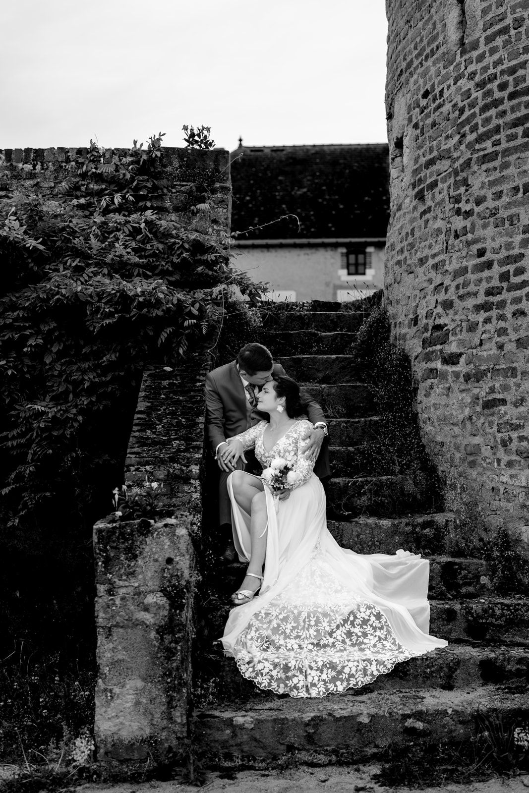 Black and white wedding photo of bride and groom sharing a romantic moment on ancient stone steps by a historic castle.