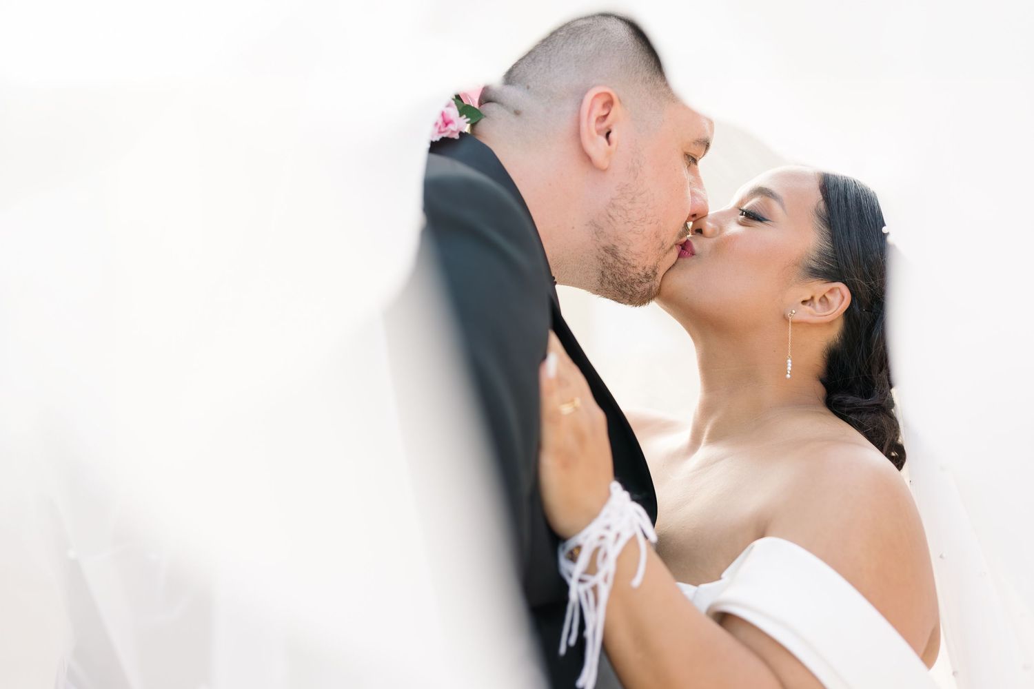 Les mariés échangent un baiser romantique le jour de leur mariage, la mariée portant une robe blanche à épaules dénudées.