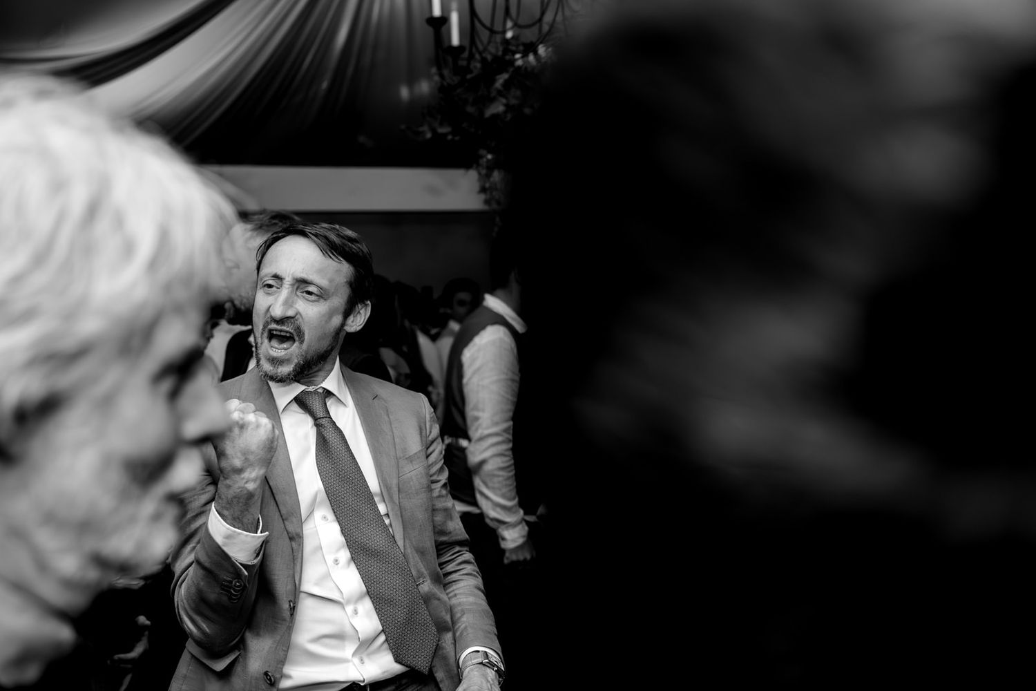 Man in suit laughing joyfully at a wedding reception in a candid black and white party photo.
