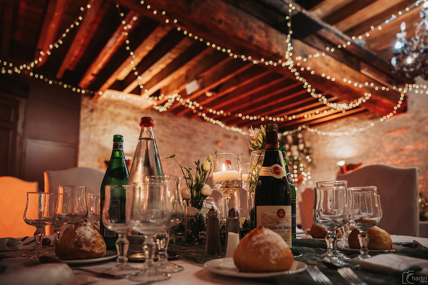 String lights and rustic wooden beams create a warm ambiance in a cozy restaurant interior.