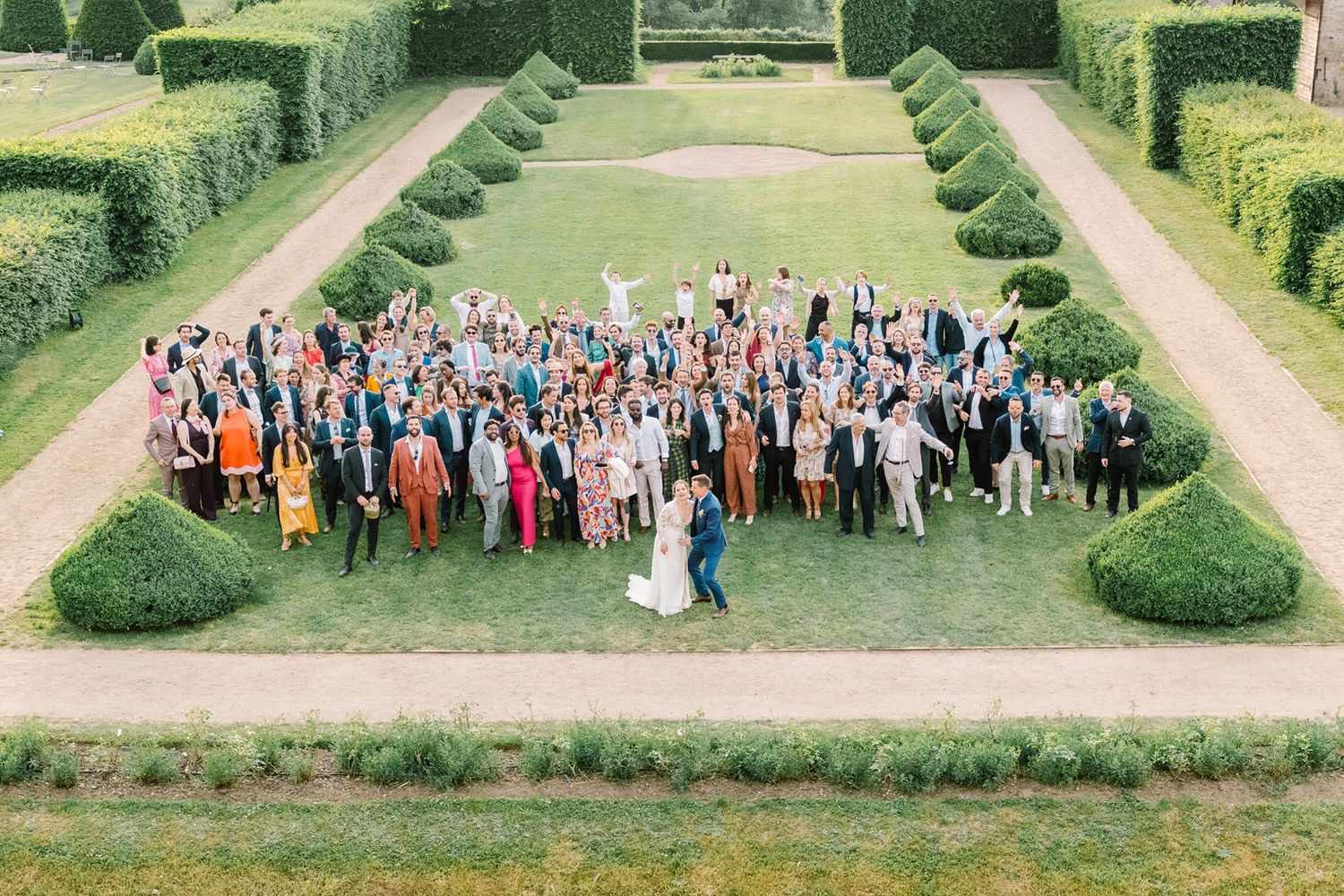 Aerial view of a large wedding group photo with guests celebrating on a manicured garden lawn.