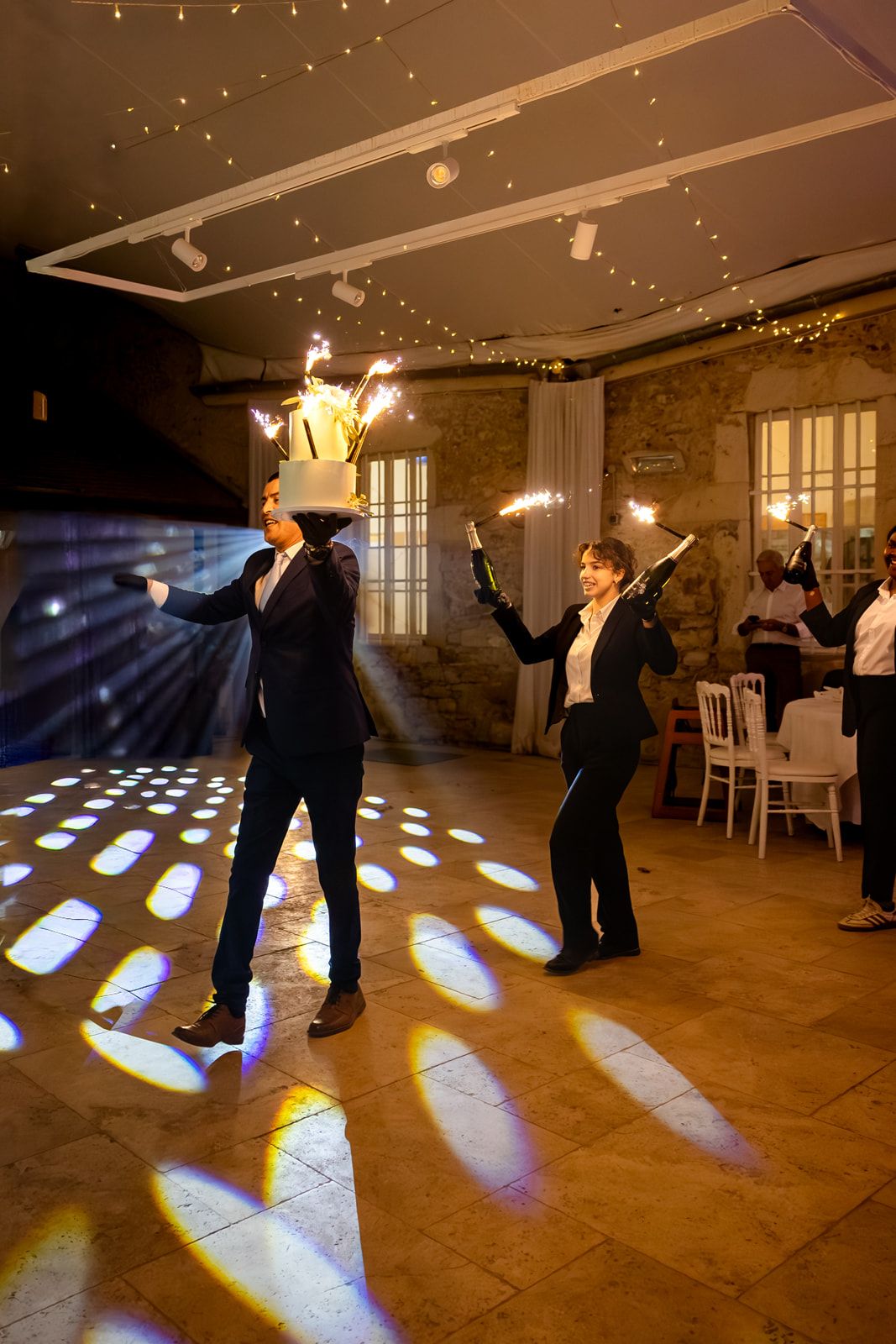 Two dancers perform an elegant dance move in a dimly lit ballroom with dramatic spotlights creating patterns on the floor.