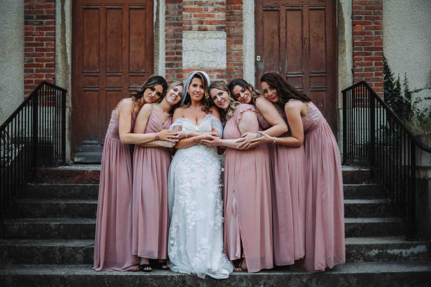 Wedding party poses on brick church steps wearing pink bridesmaid dresses.