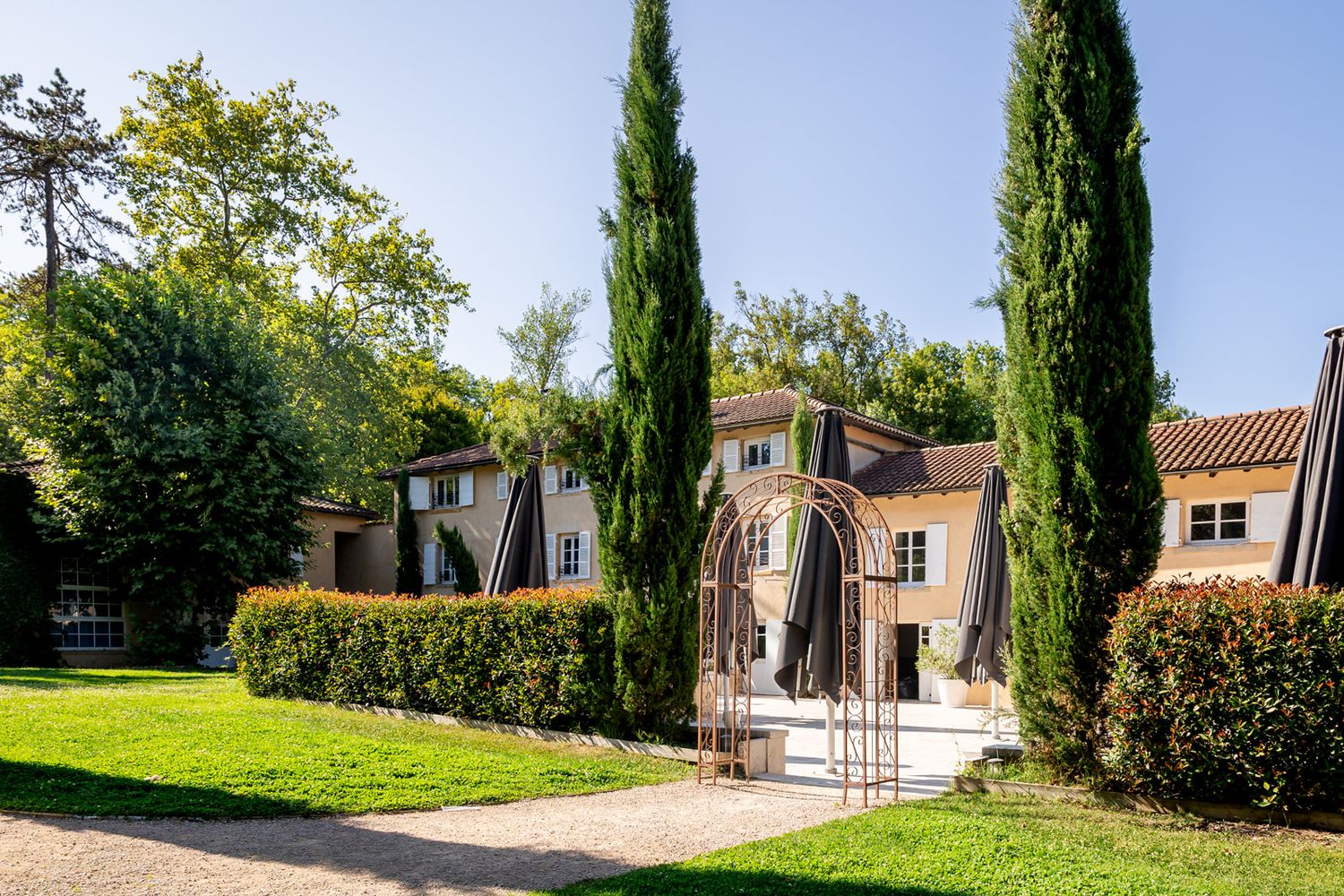 Mediterranean style villa with tall cypress trees and manicured lawn in a sunny garden setting.