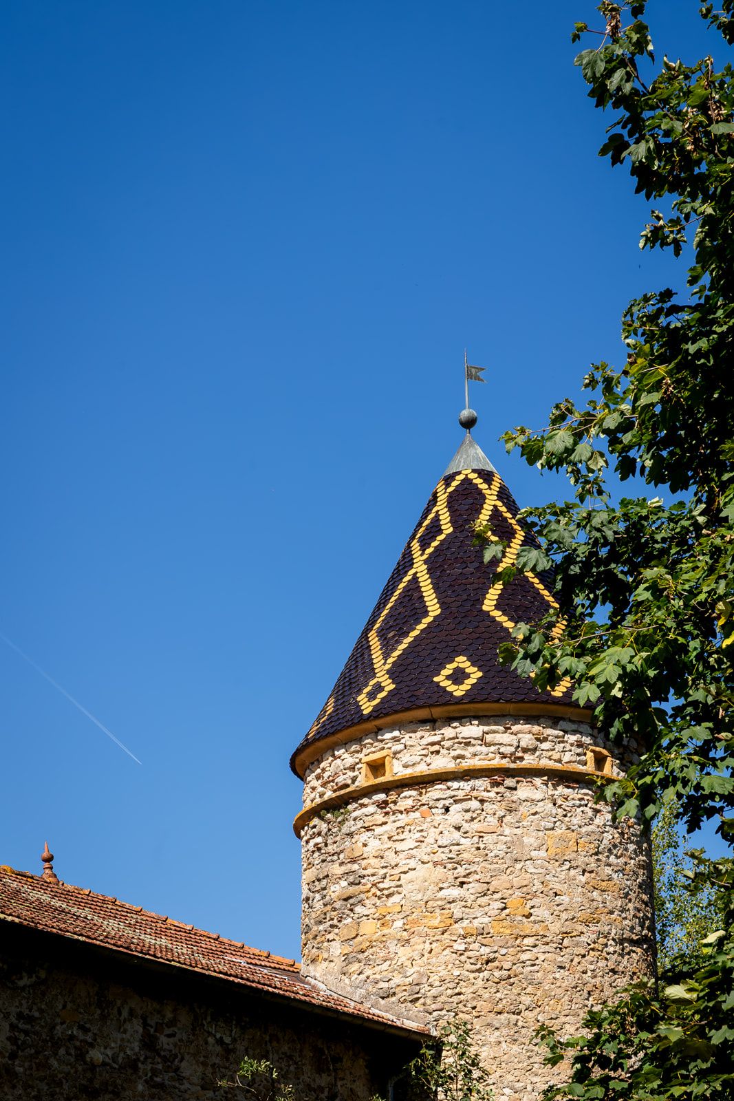 Medieval stone tower with ornate gold decorative elements atop a dark conical roof against a bright blue sky.