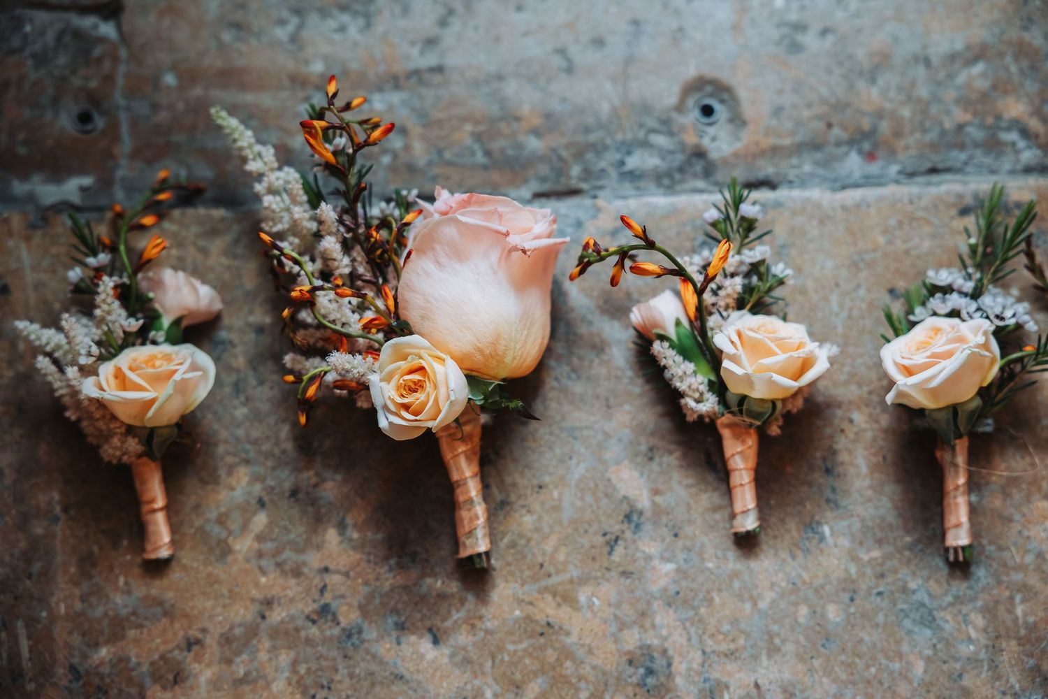 Row of delicate peach rose boutonnieres with berries on rustic surface.