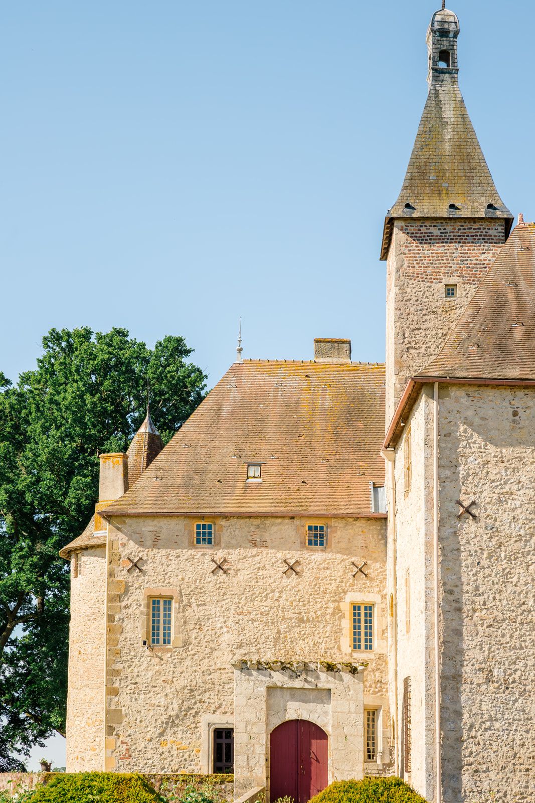 Historic French château with stone walls, terracotta roof, and pointed tower under a clear blue sky.