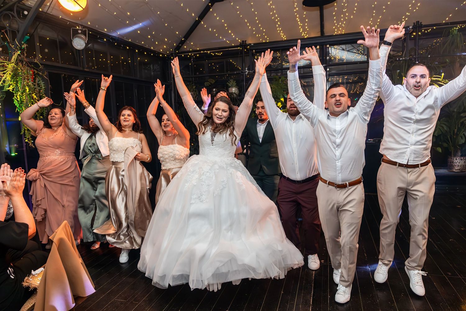 Wedding guests dance and celebrate on a lively dance floor decorated with string lights and festive decor.
