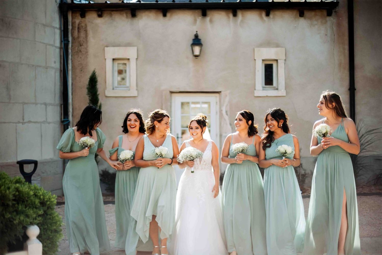 Wedding party in soft mint green dresses poses together on stone terrace.