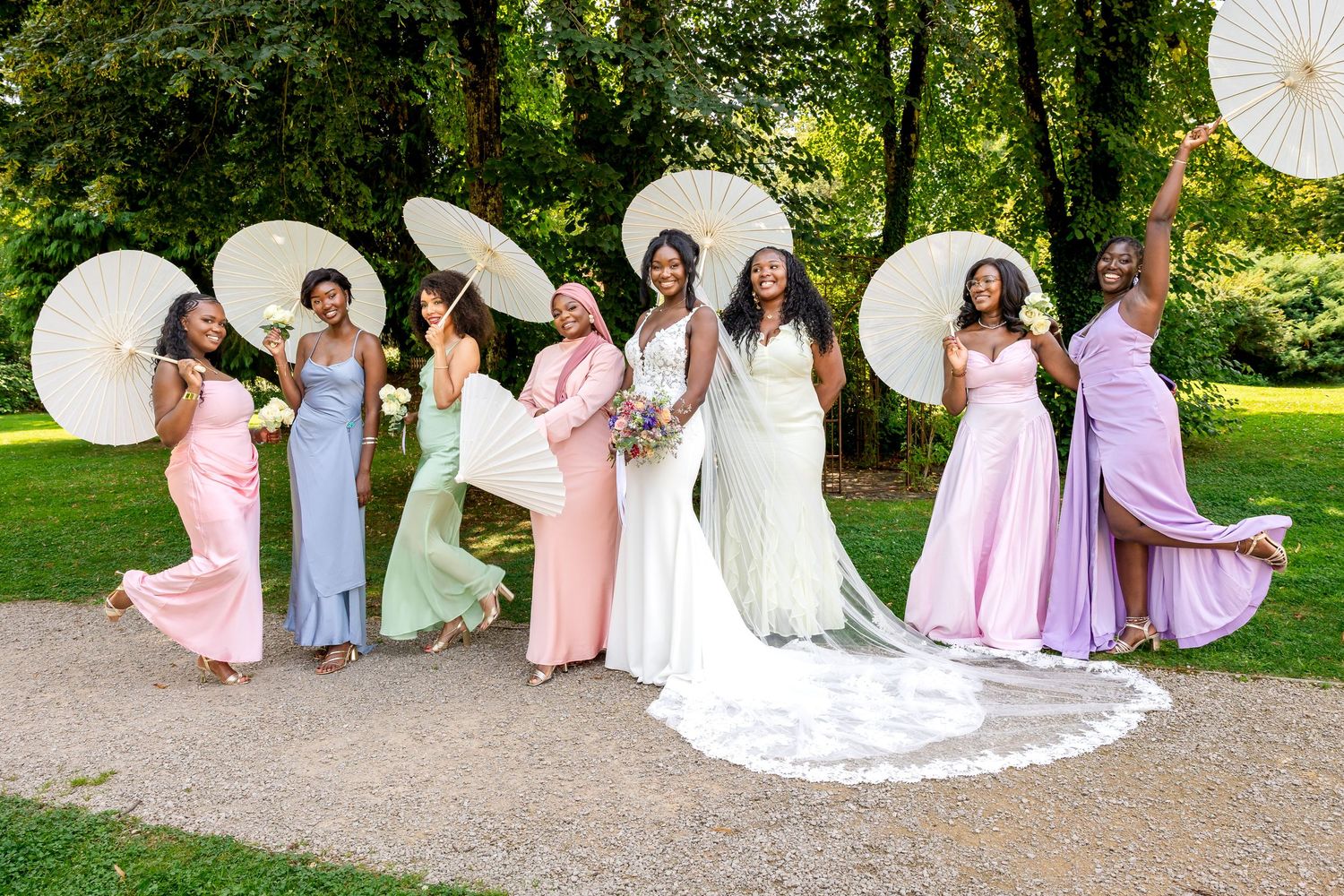 Wedding party in pastel dresses posing with parasols in a garden setting.