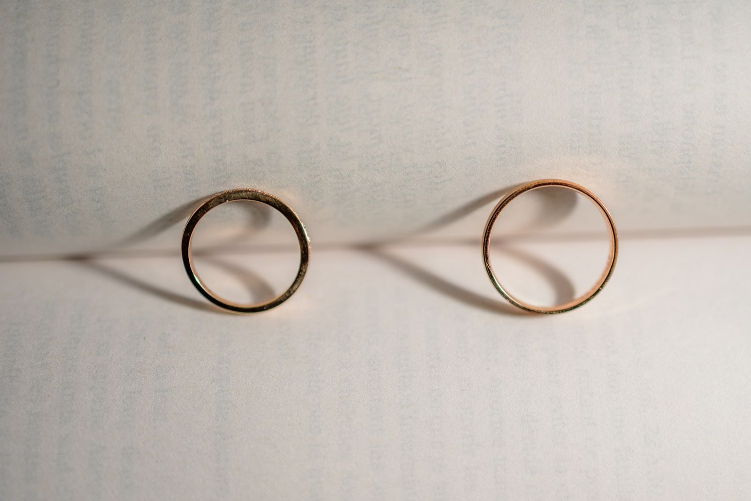 Two gold wedding bands standing upright on a white textured surface, casting elegant shadows.